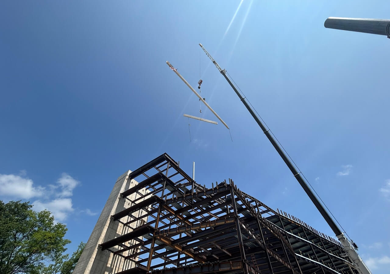 A crane places a large beam in front of a clear blue sky at the Susan Welch Building's Topping Out Ceremony.