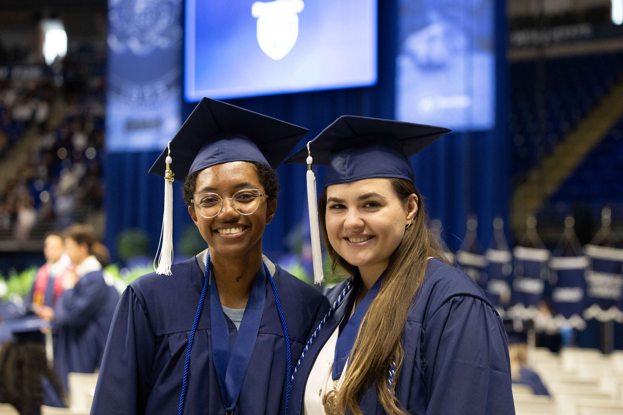 Two graduates in caps and gowns stand side by side, smiling for a photo on graduation day.