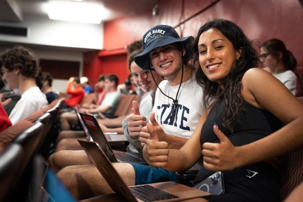 Three students smile at the camera and give thumbs up while sitting in an economics class in 121 Sparks Building.