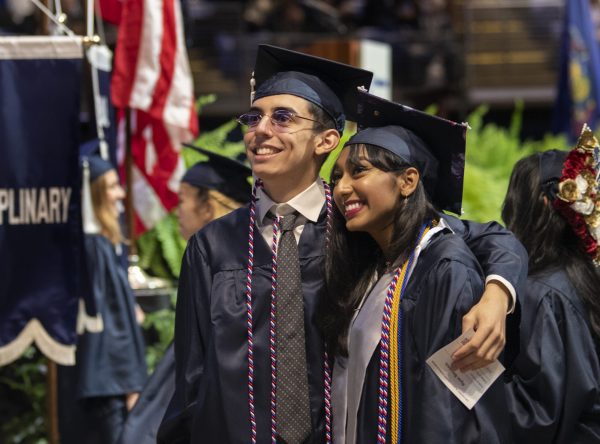 Two students dressed in academic regalia smile at someone taking their photo at the Liberal Arts commencement ceremony.