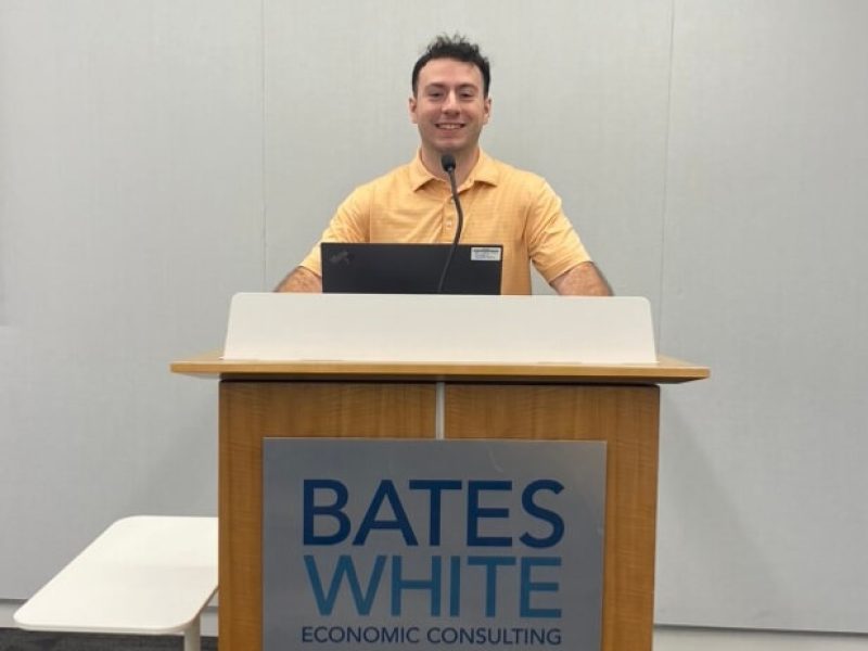 Colin Byrne, who will graduate from Penn State in 2025, stands behind a podium that reads Bates White Economic Consulting on the front.