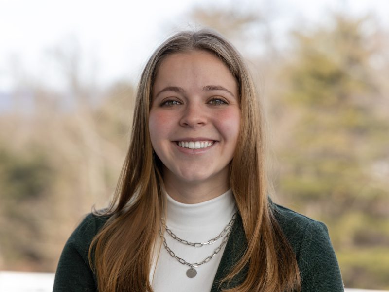 Cara graduated from Penn State in 2025 and will graduate her IUG master's degree program in 2026. She is smiling and wearing a green jacket, white turtleneck blouse and a silver necklace.