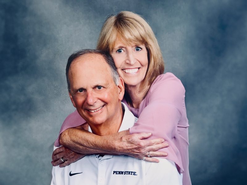A photo of David and Joanne Kleppinger, with David seated and Joanne's arms wrapped around his shoulders from behind.