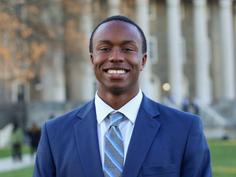 David Hayes, who will graduate Penn State in 2026, stands in a blue suit in front of Old Main at Penn State University Park.