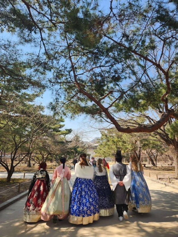 Nine students adorned in hanbok, posing in front of Gyeongbokgung Palace sites.