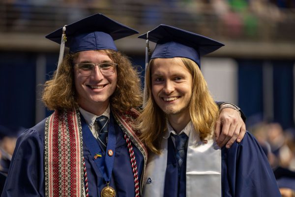 Two graduates in caps and gowns stand side by side, smiling for a photo on graduation day.
