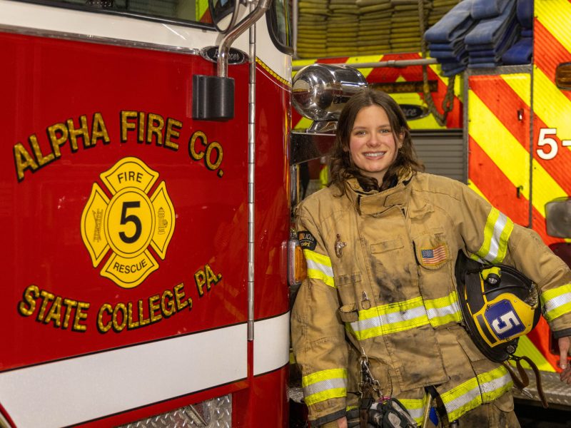 Kara Stover, who will graduate from Penn State in 2026, wears a firefighter's uniform and leans against a fire truck.