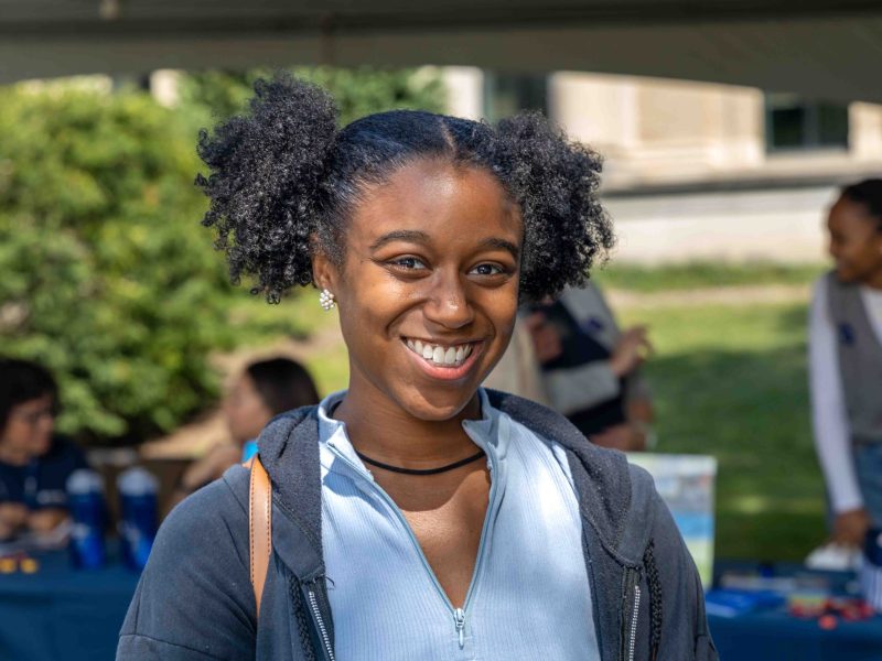 Xiomara Larkin smiles in front of informational tables on Pattee Mall during the Liberal Arts Undergraduate Festival in fall 2024.