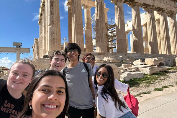 Group photo with Michelle Kengkart (center) and, left to right, Grace Pilch, Owen Perry, Mihir Kulkarni, Leila Filien, De'jah Coates, posing in front of the Parthenon in Athens, Greece.