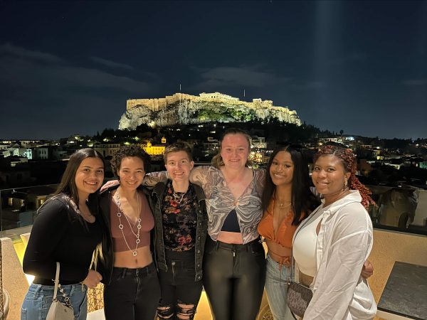 Group of Penn State students posing from a rooftop restaurant with the Acropolis, in Athens, Greece during the nightime.