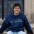 Owen Perry, who will graduate Penn State in 2026, sits on the steps of a building wearing a blue sweatshirt that says, "Thou didst mold us, Dear Old State."