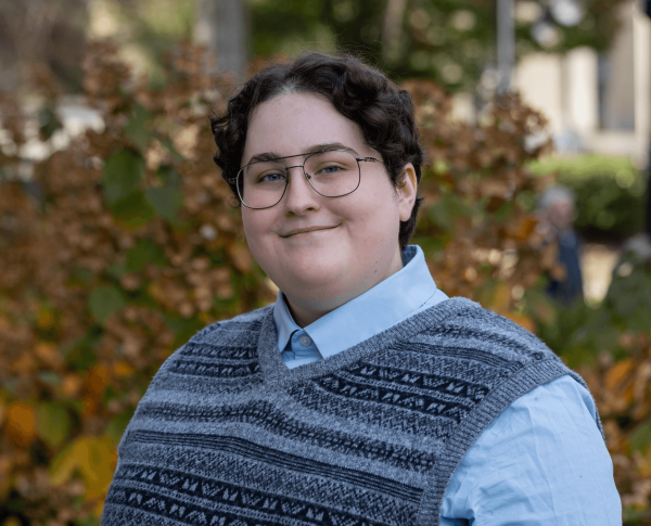 Felicity Sarnoff, who is the Penn State College of the Liberal Arts as college marshal for the fall 2024 commencement ceremony, stands in front of trees and bushes at Penn State University Park.