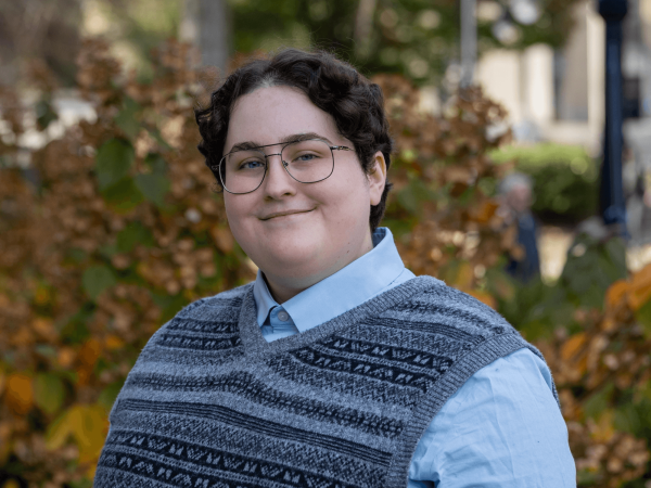 Felicity Sarnoff, who is the Penn State College of the Liberal Arts as college marshal for the fall 2024 commencement ceremony, stands in front of trees and bushes at Penn State University Park.